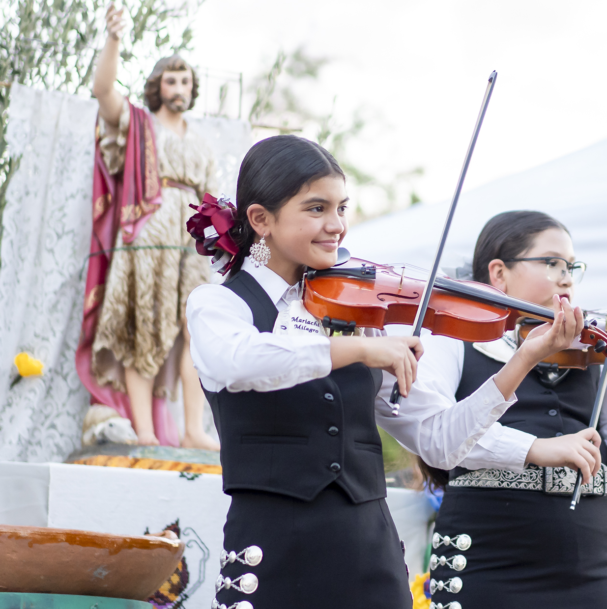 Youth mariachi in front of a statue of San Juan