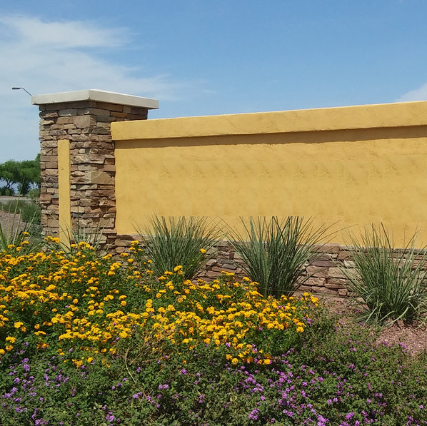 a yellow neighborhood entry monument with purple lantana and blue sky behind