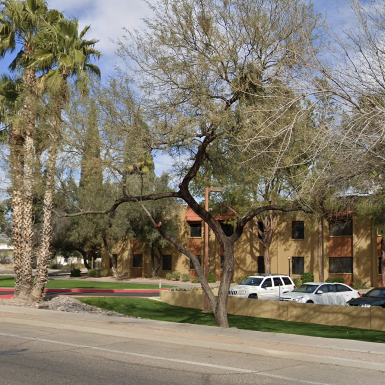 Street view of Casa de Encanto apartments - two story, block apartments with cars parked out front