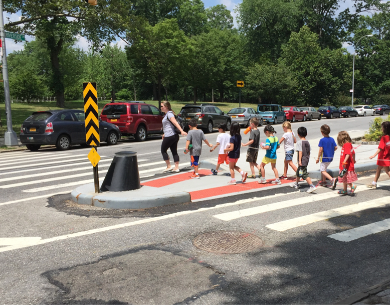 Image of a caregiver and children using a safety island as they cross a busy road. Image courtesy of www.nycstreetdesign.info)
